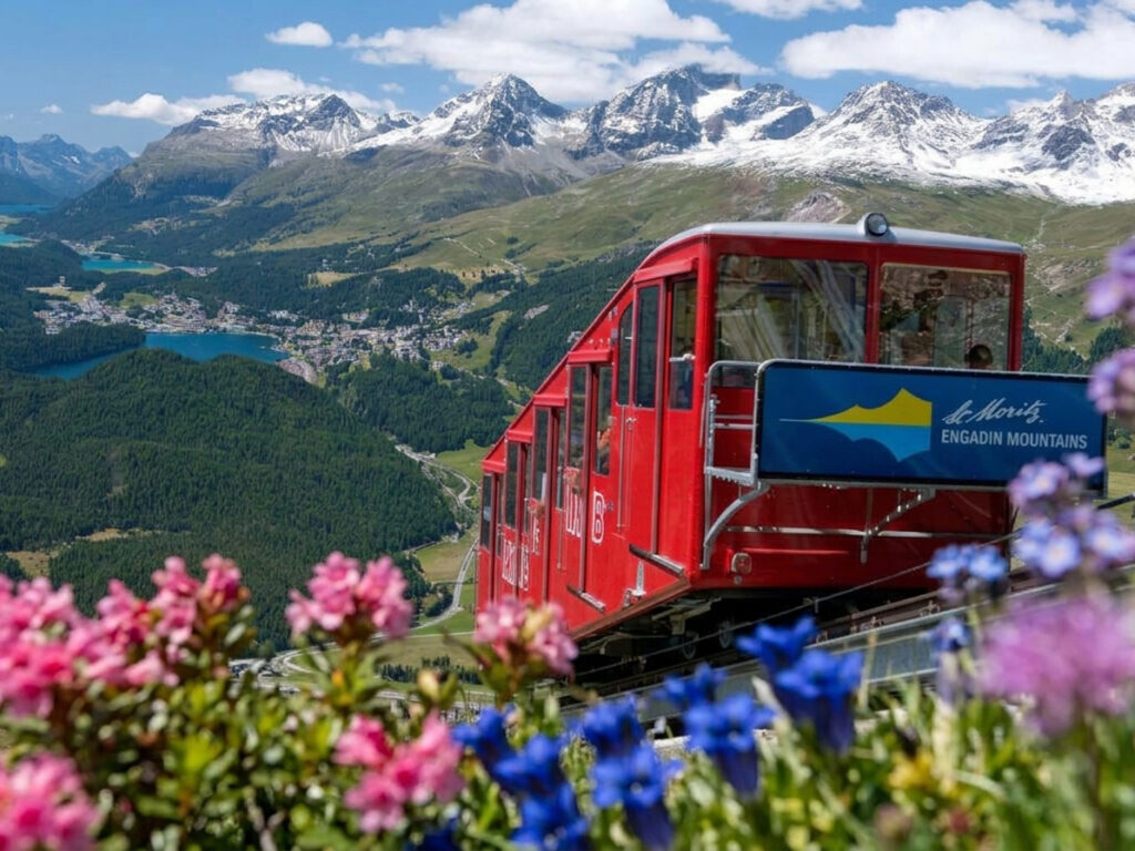 Die Bergbahn Muottas Muragl mit einen beeindruckenden Blick auf die blauen Seen, grünen Wälder und schneebedeckten Gipfel des Engadins in der Schweizer Bergwelt.